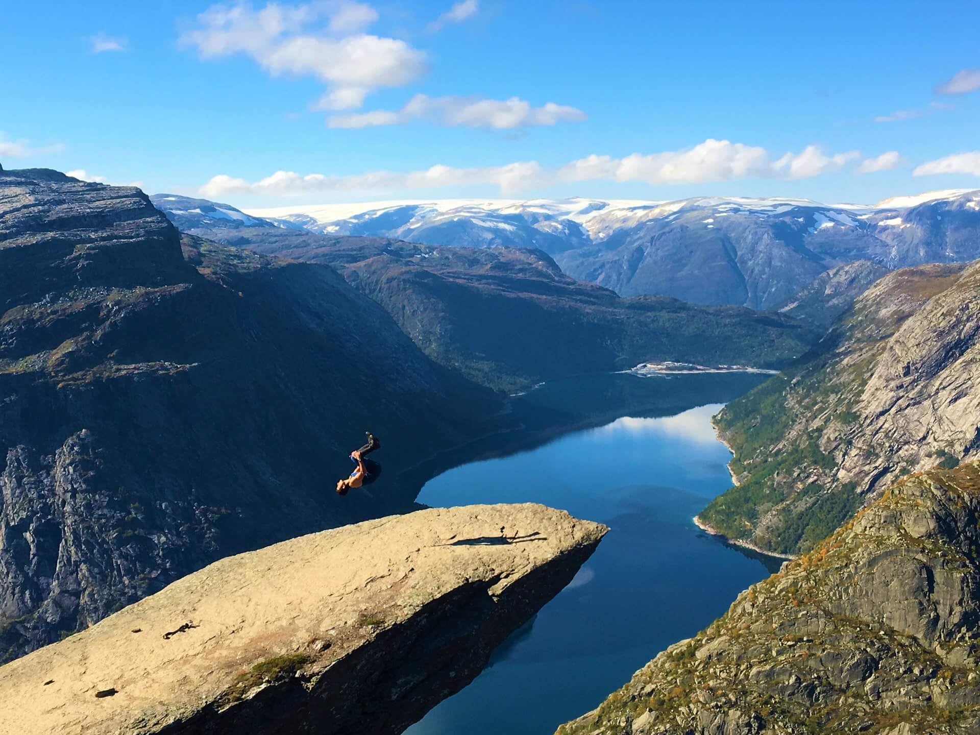 Eine Person auf einem Felsvorsprung macht einen Salto in schwindelerregender Höhe über einer weiten Berg- und Seenlandschaft